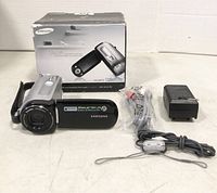 Photo showing Samsung SC-MX10 camcorder, original box, power adapter charger, AV cables, and wrist strap.