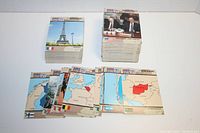 Photo showing stacks of Desert Storm Pro Set collectible cards featuring the Eiffel Tower and images of Presidents and officials, along with maps of involved countries.