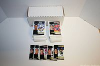 Two stacks of hockey cards in front of a white cardboard box, multiple individual cards with player images visible in front of the stacks.