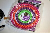 Three colorful circular plastic knitting loom rings in original packaging, sizes visible with peg design for knitting.