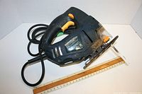 Angled side view of Mastercraft handheld jigsaw showing overall body, handle, trigger, and power cord coiled behind it. Ruler placed beside for size reference.