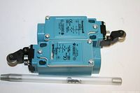 Two blue Honeywell limit switches stacked on top of each other with technical labels and roller lever actuators. Pen in foreground for size reference.