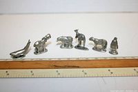 Six authentic silver-colored animal shaped Monopoly USAopoly game tokens lined up with rulers illustrating size.
