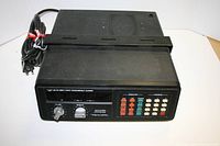 Front and top view of black Realistic model 20-112 police/fire scanner showing control knobs, multicolored push buttons, and mounting rack with attached power cord.