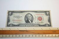 Front of 1953 Series $2 banknote with red seal, portrait of Thomas Jefferson, red serial number 02093184A, on a white background with ruler for scale.
