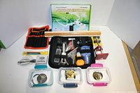 Wide shot showing full assortment of watch repair tools, parts containers, and pocket watch with rulers for scale.