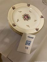 Stack of four ceramic cake plates with cream background, floral center design, and gold rim.