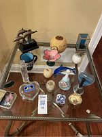 Top-down view showing assortment of decorative items on glass table including dolphin figurine, carved gourd, stained glass flowers, bells, and ceramic pieces.