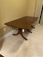 Full view of the wooden dining table fully extended, showing the three pedestal legs and smooth wooden top surface.