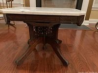 Side view of antique coffee table showing dark wood carved base and legs supporting white marble top
