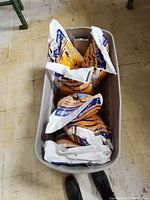 Six orange and blue Road Runner Rock Salt bags in a container, one is visibly open.