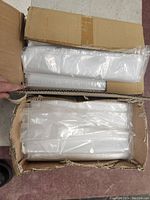 Two open cardboard boxes filled with large clear ziplock bags wrapped in plastic packaging.