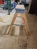 Side view showing two wooden legs with metal brace, top step with metal reinforcement at corners