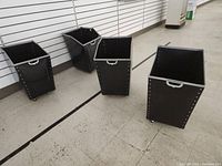 Four black plastic totes with riveted edges, handles, and wheels positioned on a store floor.