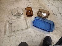 View of bakeware items on floor showing five glass pieces including clear, amber, and blue-tinted pieces.