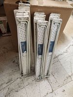 Stack of 17 packaged white double curtain rods leaning against a box.