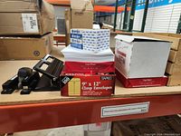 Photo showing three reams of copy paper, two sealed, one opened, two boxes of clasp envelopes and some office tools