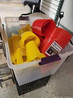 Large plastic bin filled with yellow and red plastic paint trim cups with integrated handles stacked inside.