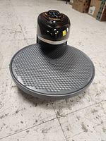 Side view of black pizza oven with gray rotating cooking pan on floor