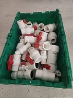 Green tote box filled with various white PVC valves and fittings, many with red handles visible.