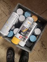 Overhead view of multiple spray paint cans in a crate showing various cap colors including white, blue, and yellow.