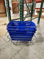 Stack of three blue plastic shopping baskets resting in one wire metal holder, showing how baskets fit inside the holder.