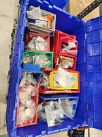 Photo of a large blue tote filled with several small colored bins containing assorted hardware including hinges and knobs, all organized and bagged.