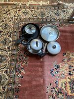 Photo of cookware: one 12" stainless steel saucepan with lid, black cast iron skillet, two smaller stainless steel saucepans with lids.