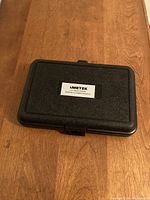 Closed black plastic carrying case for Ametek Digital Tachometer Gauge with white label