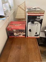 Photo of two boxed appliances on wooden surface: Hamilton Beach 10-Speed Blender and KitchenAid Real Feeder Juicer.