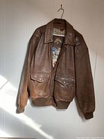 Front view of brown genuine leather Army Air Corp. flight jacket with two front flap pockets, zipper closure, and ribbed cuffs and waistband.