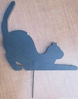 Black wooden black cat yard ornament silhouette showing front side which depicts the cat stretching with tail curved upwards, attached to a steel post.