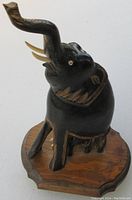 Side view showing carved elephant with raised trunk and tusks, mounted on wood base.