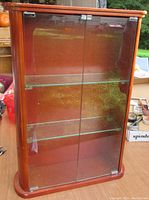 Front view of light cherry wood cabinet with two glass doors and two glass shelves inside, showing used condition.