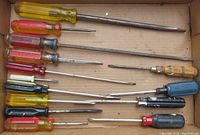 Top view of fourteen screwdrivers laid out flat in a cardboard box, showing variety in handle colors and shaft lengths.