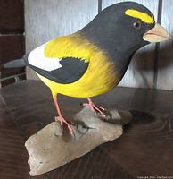 Front and side view of the hand carved wood oriole bird figurine mounted on a natural wood base, showing painted yellow and black feathers and white wing patch.
