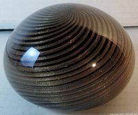 Side view of Murano art glass paperweight showing gold swirl over bronze center with glossy finish.