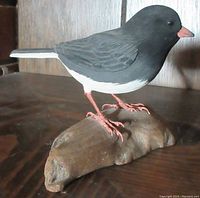 Side view of hand carved wooden Slate Junco bird standing on naturalistic base, highlighting overall shape, color and craftsmanship.