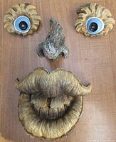 Front view of the 4 pieces arranged on a wooden surface to form a face with two eyes, a nose and a mouth, showing carving and painted detail