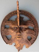 Front view showing the leaf-shaped sun dial face with human facial features and Roman numerals around the edges.