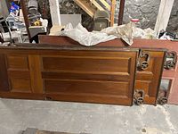 Four wooden antique pocket doors stacked lying flat, showing panelled designs and wood finish.