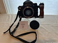 Front view showing camera body, wooden side grip, open lens mount, body cap placed beside and attached strap.