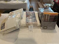 Photo shows all items: thermal cotton blanket, duvet set, sheet set and curtain package laid out on a table.