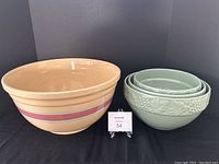 Front view of the large beige ceramic bowl with pink and red stripes alongside the set of three mint green nested ceramic bowls with embossed fruit decoration.