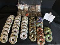 Disc-shaped cloisonné pendants arranged in rows by color; floral motifs on white, green, red, blue, and black bases.