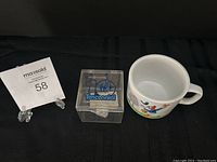 Photo showing clear Tenccennial candy box next to vintage Donald Duck mug and auction lot number card