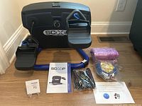 SCOOP SC100 lateral trainer with foot pedals, assembly manual, resistance bands, jump rope, purple balance form exercise ball, and instructions on floor.