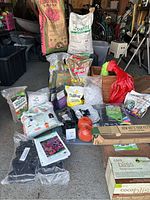 Photo showing a variety of gardening supplies including large bags of soil amendments and fertilizers, gardening twine, seed packets, and fabric containers.