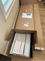 Open cardboard box containing flat white part boxes and a long narrow box, showing unassembled metal components.