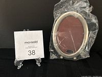 Front view of unopened oval sterling silver picture frame in original plastic wrap showing shape and label.